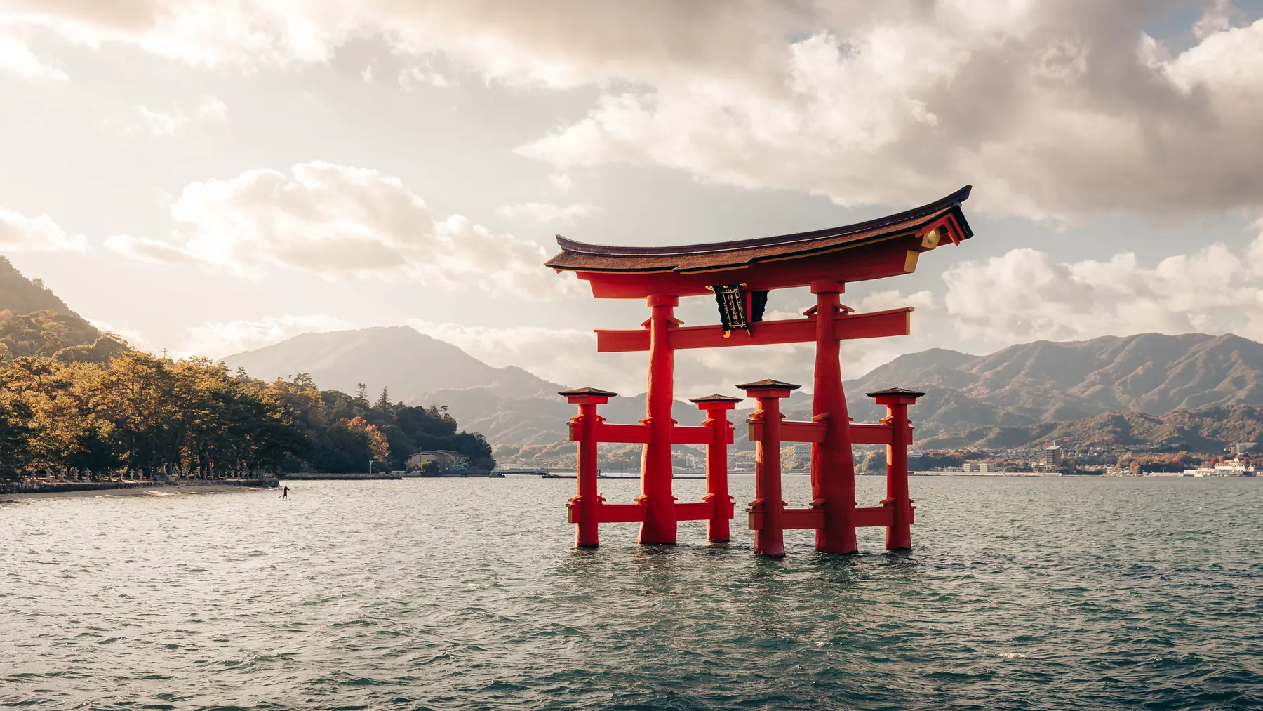 Torii vermelho de Itsukushima em pé na água, com montanhas atrás